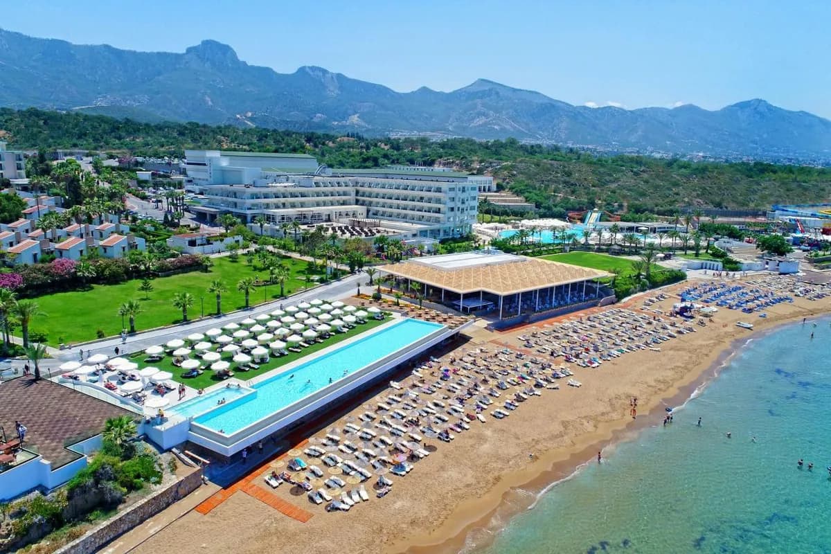 Hotel Acapulco Resort na Cyprze Północnym z lotu ptaka: piaszczysta plaża z leżakami, długi basen nad morzem i pasmo gór Kyrenii w tle