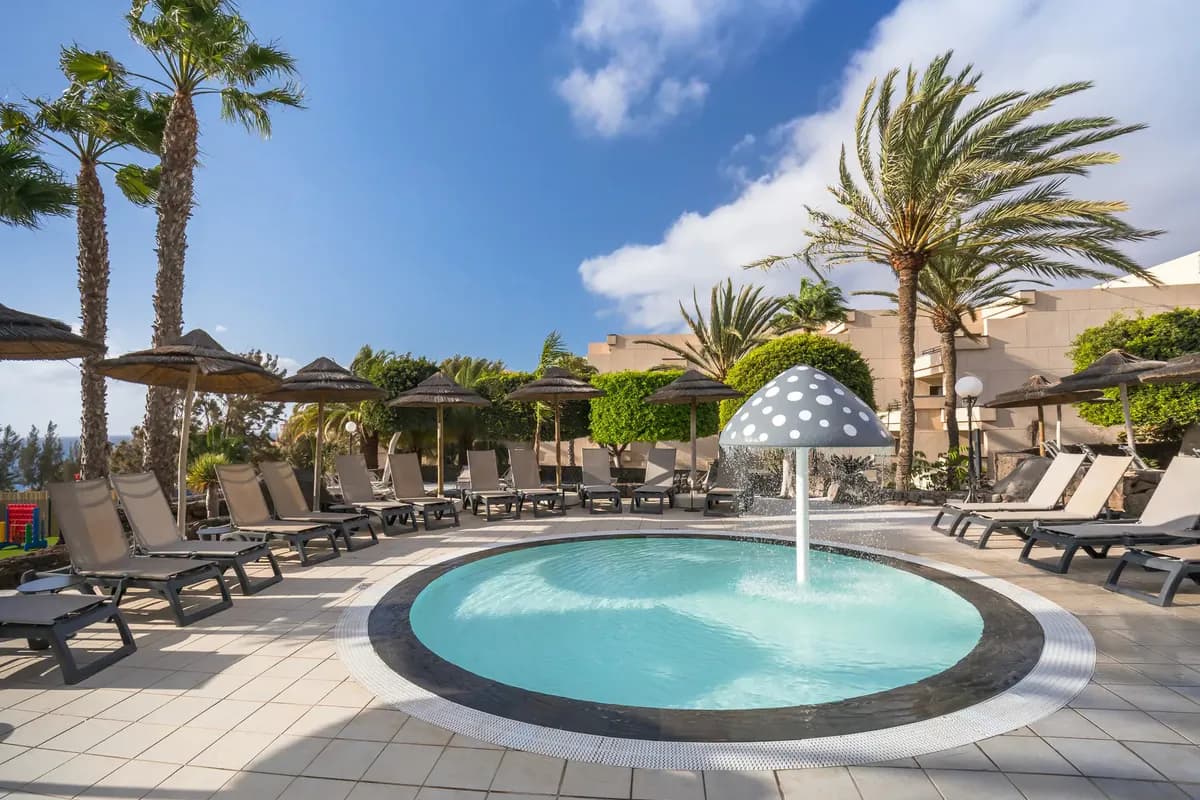 Okrągły, płytki brodzik z fontanną w kształcie grzyba w hotelu Barceló Lanzarote Active Resort, wokół leżaki i palmy