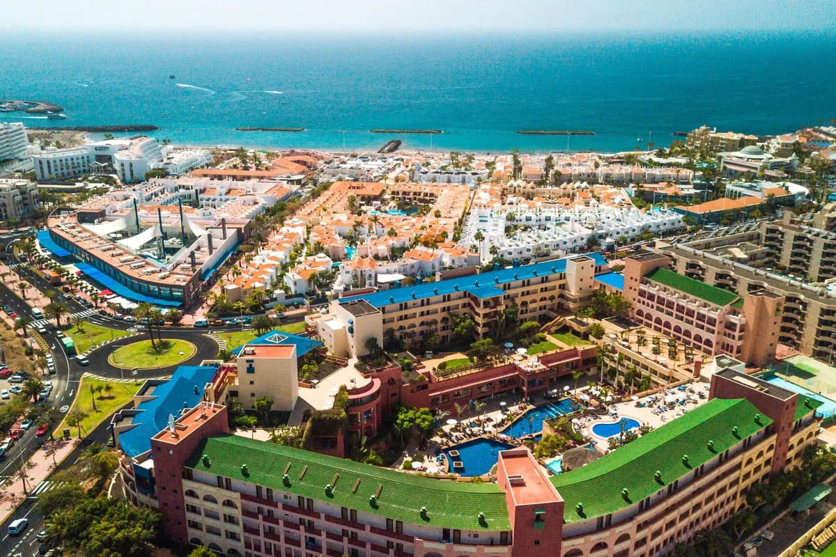 Costa Adeje na południu Teneryfy z lotu ptaka: hotele z basenami, biała zabudowa i plaża osłonięta falochronami nad oceanem
