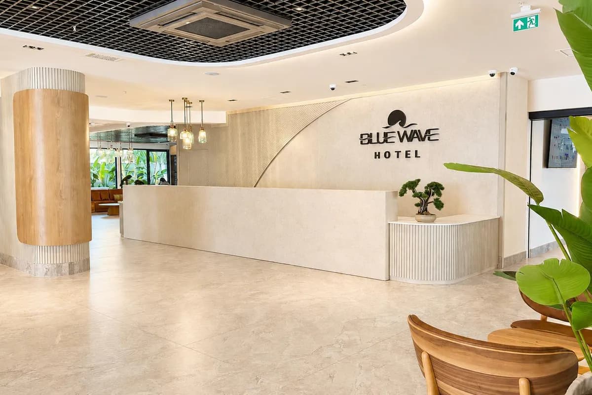 Jasna recepcja hotelu Blue Wave Suite na Riwierze Tureckiej z kamiennym kontuarem i logo hotelu na ścianie