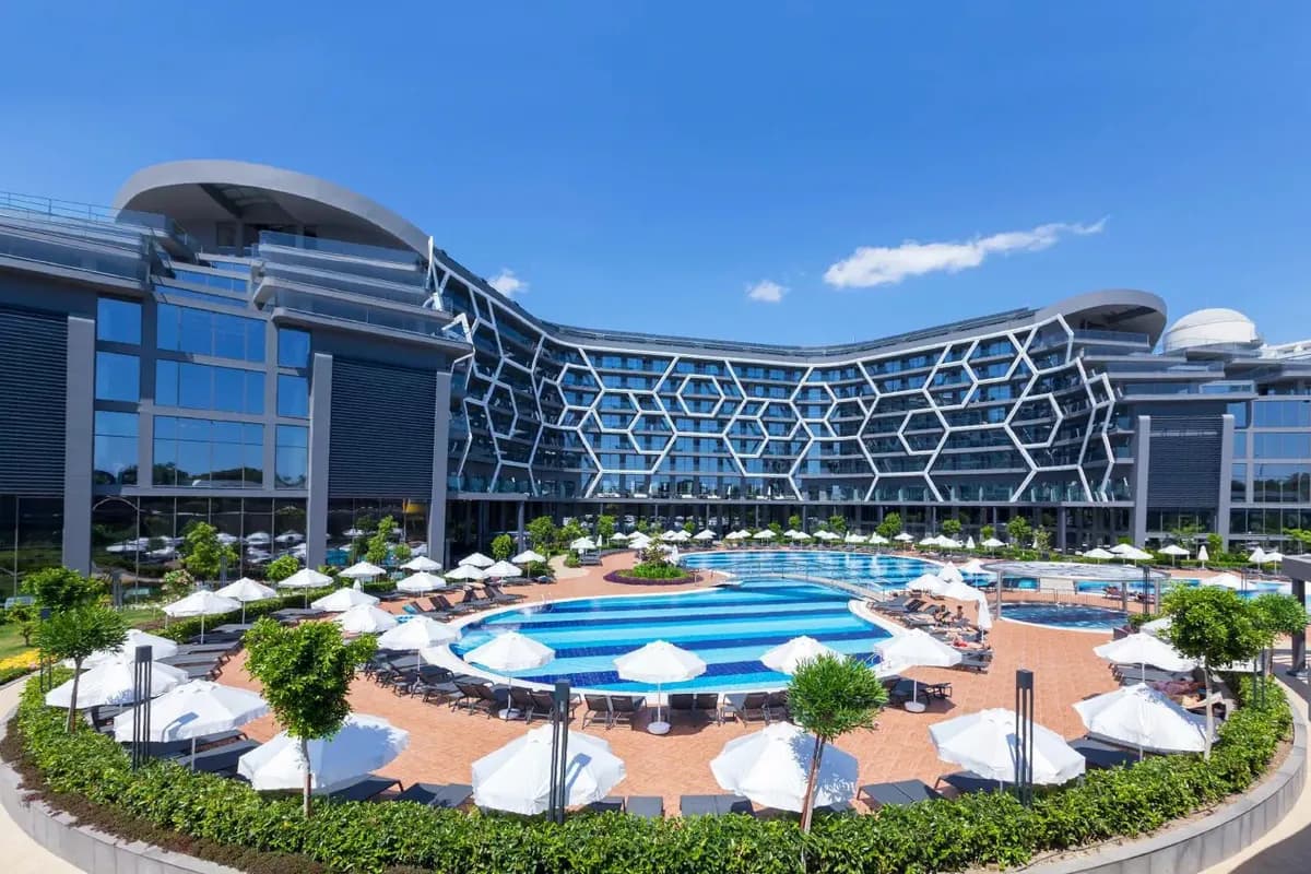 Basen otoczony białymi parasolami i leżakami przed nowoczesnym budynkiem hotelu Bosphorus Sorgun w Turcji