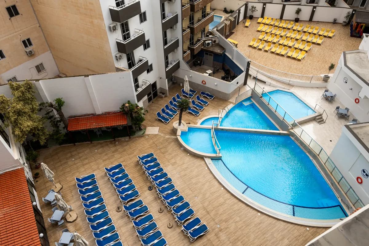 Widok z góry na dziedziniec hotelu Canifor w St. Paul's Bay na Malcie: baseny otoczone rzędami niebieskich i żółtych leżaków między budynkami