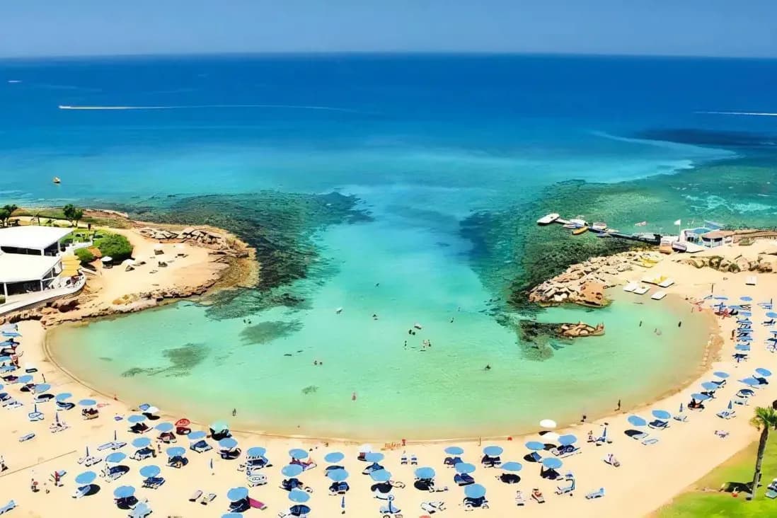 Piaszczysta zatoka w Protaras na Cyprze z turkusową wodą, skalistymi cyplami i rzędami parasoli na plaży