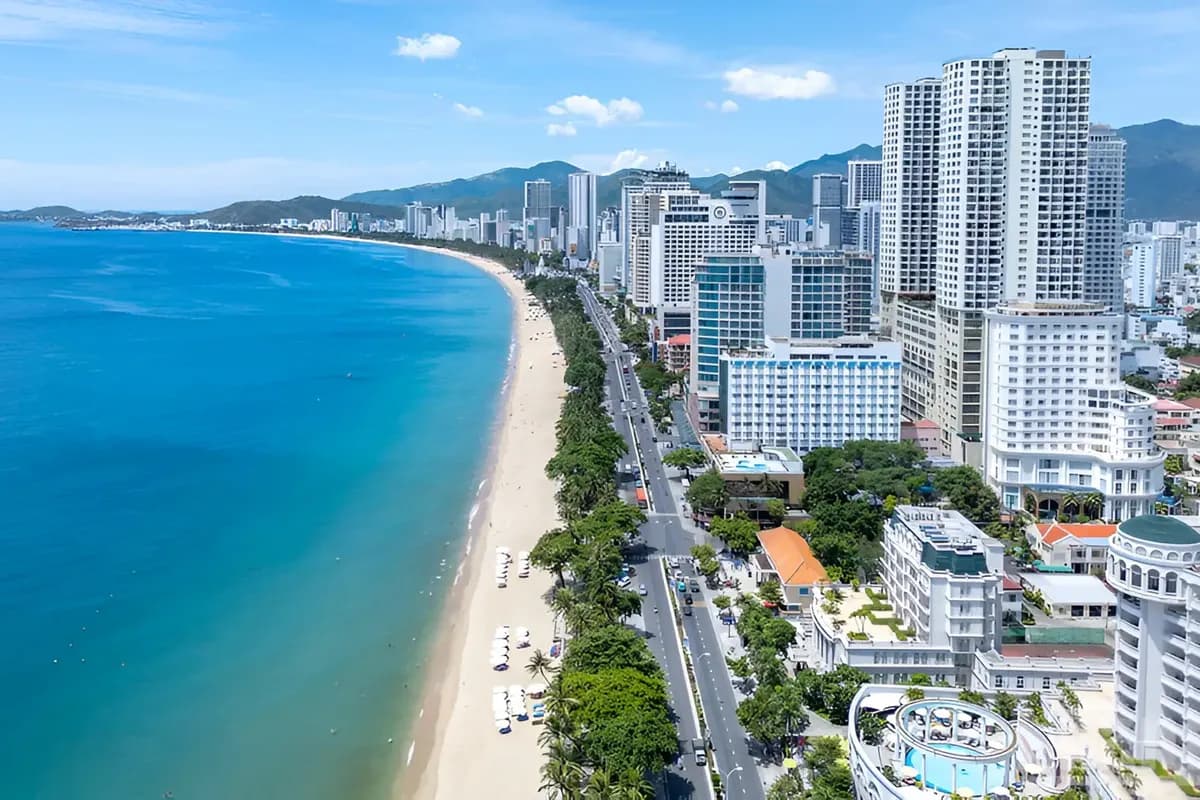 Widok z góry na zatokę Nha Trang w Wietnamie: długa piaszczysta plaża, nadmorska aleja z drzewami, wysokie hotele i góry w tle