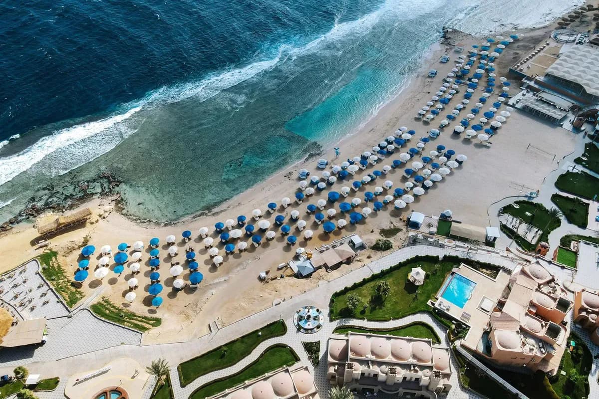 Widok z lotu ptaka na plażę hotelu Diamond Beach by Pearl Resort nad Morzem Czerwonym w Egipcie, z niebieskimi i białymi parasolami