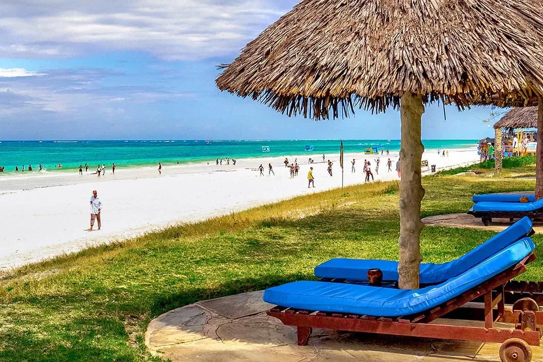 Biała piaszczysta plaża Diani w Kenii z turkusowym oceanem, leżakami i parasolem krytym strzechą na pierwszym planie