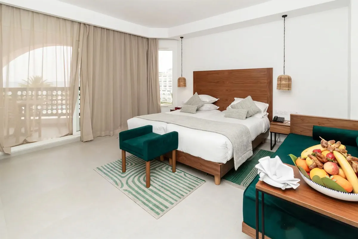Pokój w hotelu El Mouradi Palm Marina w Port El Kantaoui: łóżko z drewnianym zagłówkiem, wiklinowe lampy, telefon i gniazdka przy szafce nocnej