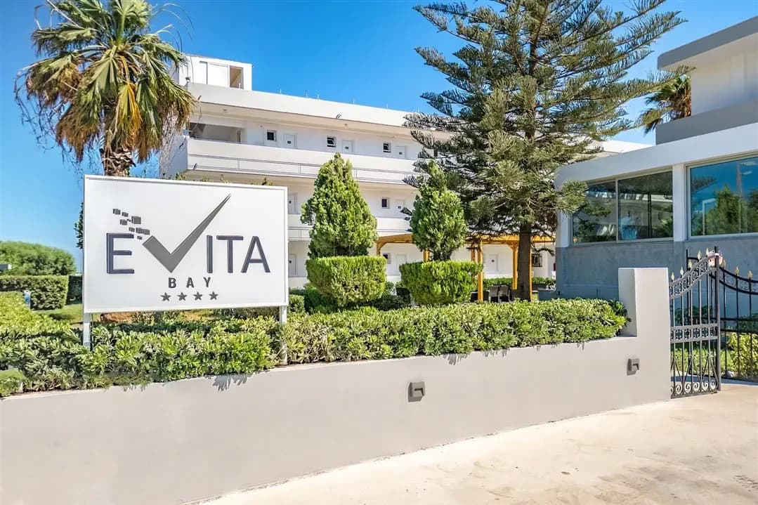 Tablica z nazwą hotelu Evita Bay i czterema gwiazdkami przed białym budynkiem hotelowym w Faliraki na Rodos, obok palma i araukaria