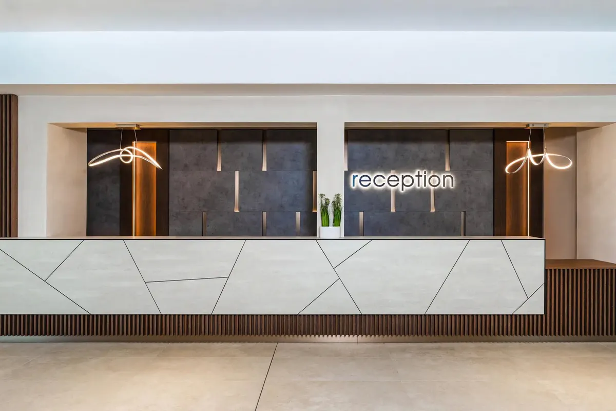 Recepcja hotelu Festa Panorama w Nesebyrze: jasna lada z geometrycznym wzorem i podświetlony napis „reception” na ciemnej ścianie