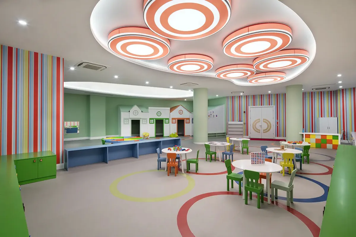 Przestronna sala miniklubu w hotelu Granada Luxury Beach w Avsallar: kolorowe stoliki i krzesełka, domki do zabawy i pasiaste ściany