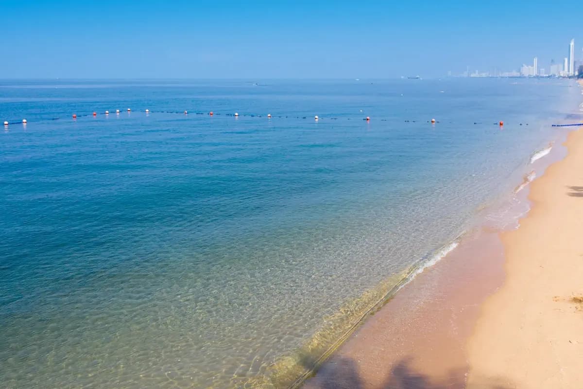 Plaża hotelu Mövenpick Siam Na Jomtien: płytka, przejrzysta woda, linia boi wyznaczająca kąpielisko i wieżowce Pattayi na horyzoncie