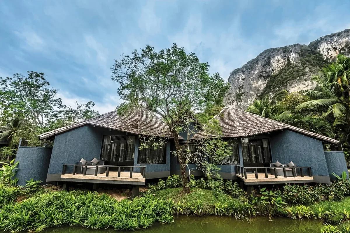 Wille hotelu Peace Laguna w prowincji Krabi nad stawem, otoczone bujną zielenią, pod wapienną skałą i zachmurzonym niebem