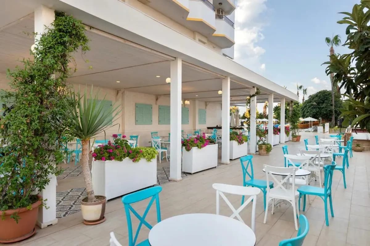 Zadaszony taras restauracji hotelu Prestige Alanya w Turcji z białymi i turkusowymi krzesłami oraz kwiatami w donicach