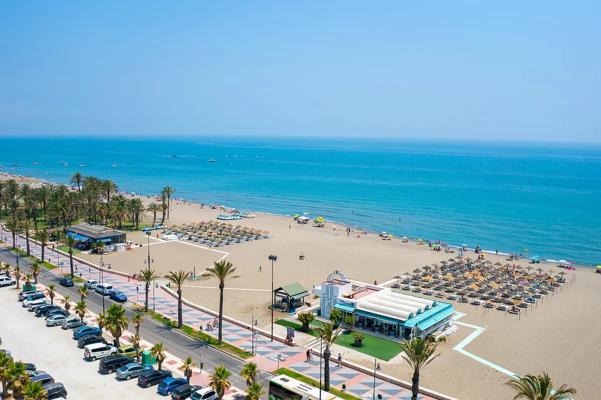 Szeroka, piaszczysta plaża w Torremolinos z rzędami leżaków, nadmorska promenada obsadzona palmami i turkusowe morze