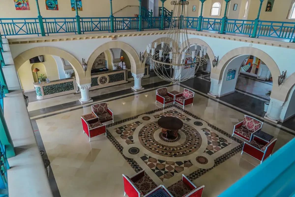 Lobby hotelu Regency Monastir w Tunezji: arkady z łukami, posadzka z geometryczną mozaiką, duży żyrandol i czerwone fotele, widok z antresoli