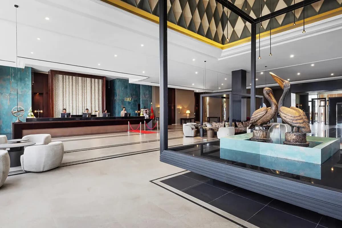 Recepcja hotelu Riu Palace Tikida Agadir w Maroku: długa lada z pracownikami, jasne lobby i fontanna z rzeźbami dwóch pelikanów