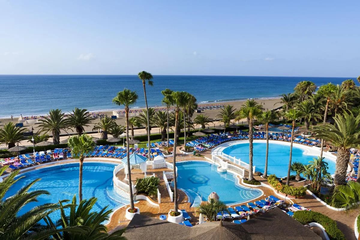Baseny wśród palm w hotelu Sol Lanzarote w Puerto del Carmen, a za nimi szeroka, piaszczysta plaża z leżakami i spokojny Atlantyk