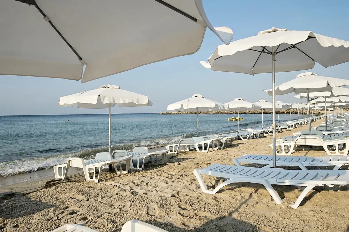 Piaszczysta plaża hotelu Sol Nessebar Bay & Mare w Bułgarii: białe parasole i leżaki, fale Morza Czarnego i falochron w oddali