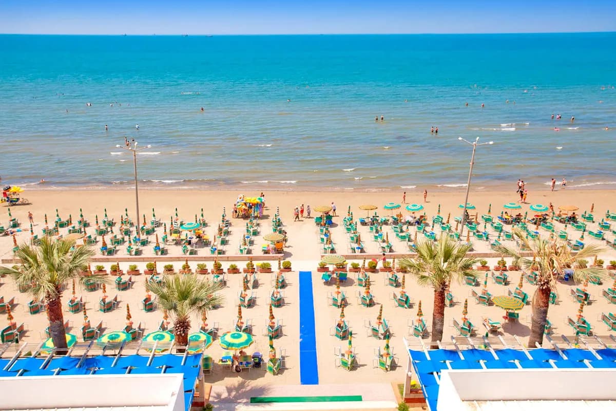 Widok z hotelu Sun w Durres: niebieski chodnik prowadzi przez plażę z rzędami parasoli i leżaków prosto do morza