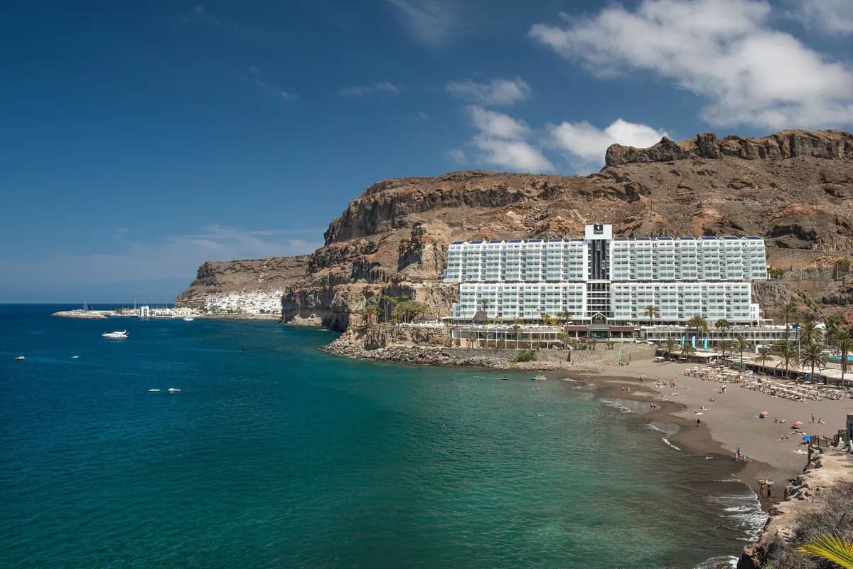 Hotel Taurito Princess u stóp brązowych skał nad zatoką Taurito na Gran Canarii, z ciemną piaszczystą plażą i turkusowym oceanem
