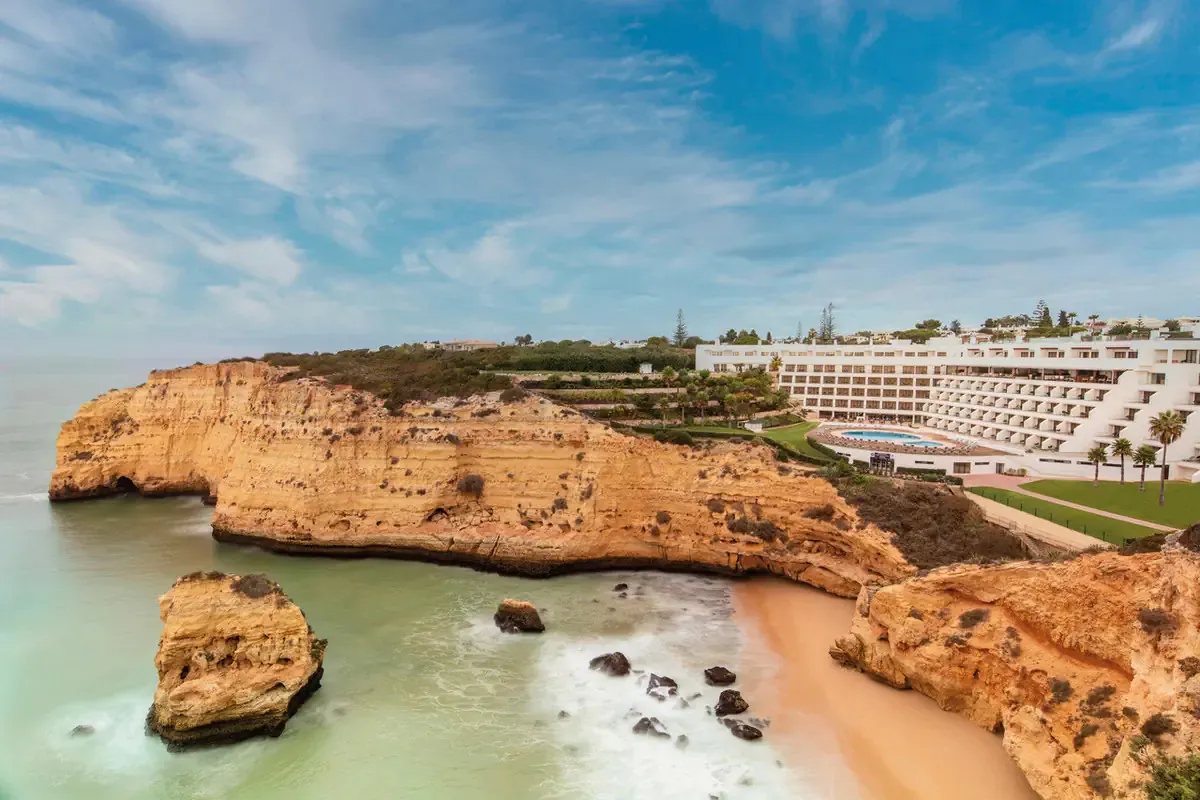 Hotel na złocistych wapiennych klifach nad niewielką piaszczystą zatoką w Carvoeiro w Algarve, na pierwszym planie skała wystająca z oceanu