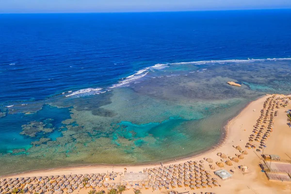 Widok z lotu ptaka na rafę koralową przy brzegu i piaszczystą plażę z parasolami przy hotelu Utopia Blue w regionie Marsa Alam