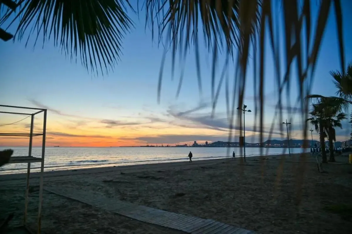Szeroka piaszczysta plaża w Durres o zachodzie słońca, z palmami i widokiem na miasto w oddali