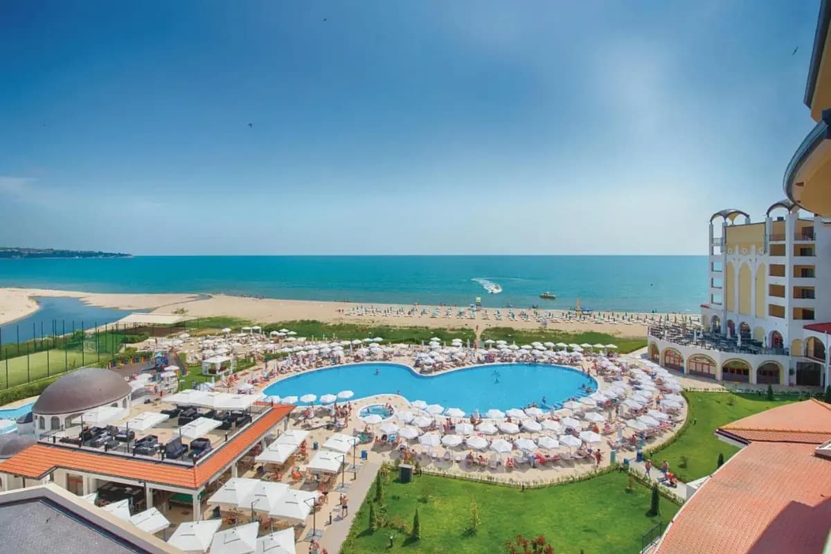 Widok z góry na basen otoczony białymi parasolami i szeroką piaszczystą plażę przy hotelu Alua Helios Bay w Obzorze w Bułgarii