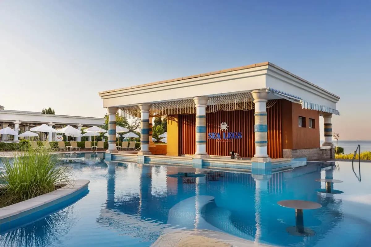 Bar w basenie hotelu Alua Sunny Beach Resort & Spa w Słonecznym Brzegu, z hokerami ustawionymi w wodzie i kolumnami w biało-niebieskie pasy