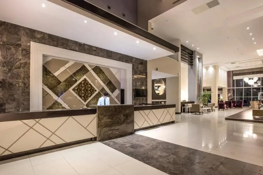 Recepcja hotelu Aria Claros w Turcji: pracownik za kamienną ladą i jasne, przestronne lobby