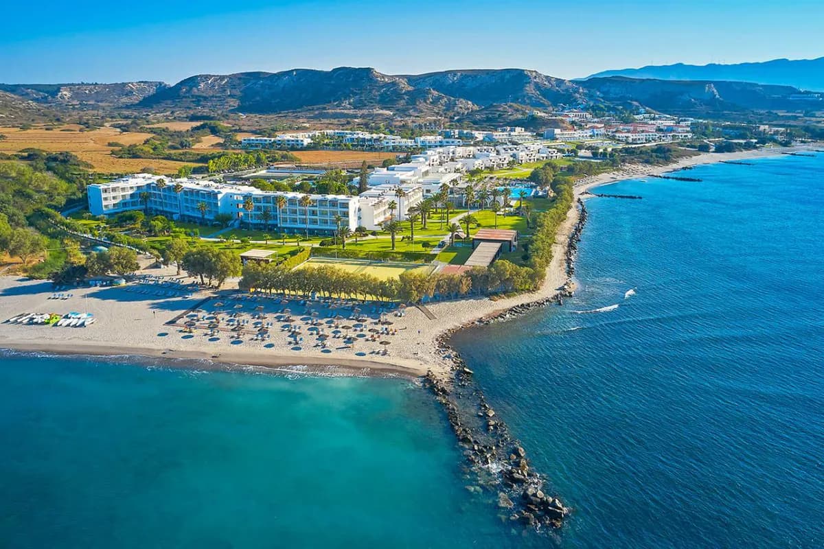 Kompleks hotelowy w okolicach Kardameny na Kosie z lotu ptaka: zielony teren z palmami, plaża z parasolami, kamienny falochron i wzgórza w tle