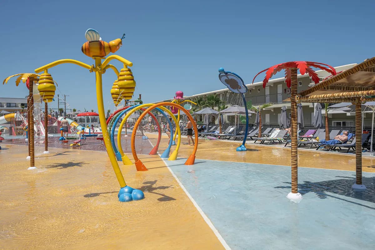 Wodny plac zabaw hotelu Caretta Paradise na Zakynthos: kolorowe łuki i fontanny na płytkim brodziku, w tle leżaki i budynek hotelu