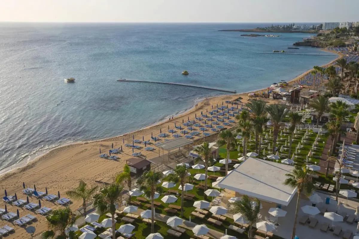 Piaszczysta plaża w Protaras na Cyprze z rzędami parasoli, palmami i hotelowym ogrodem nad spokojnym morzem