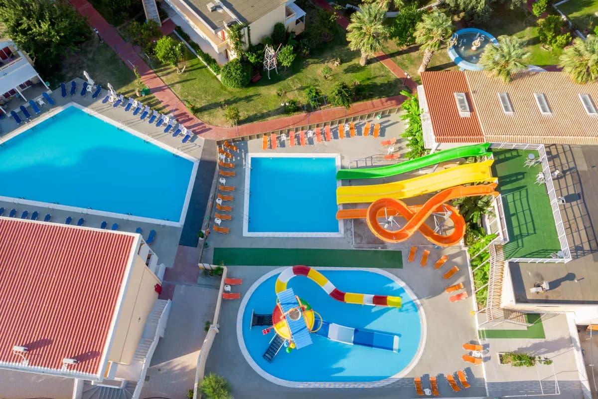 Baseny i kolorowe zjeżdżalnie hotelu Golden Odyssey w Kolymbii na Rodos z lotu ptaka, obok brodzik z wodnym placem zabaw dla dzieci