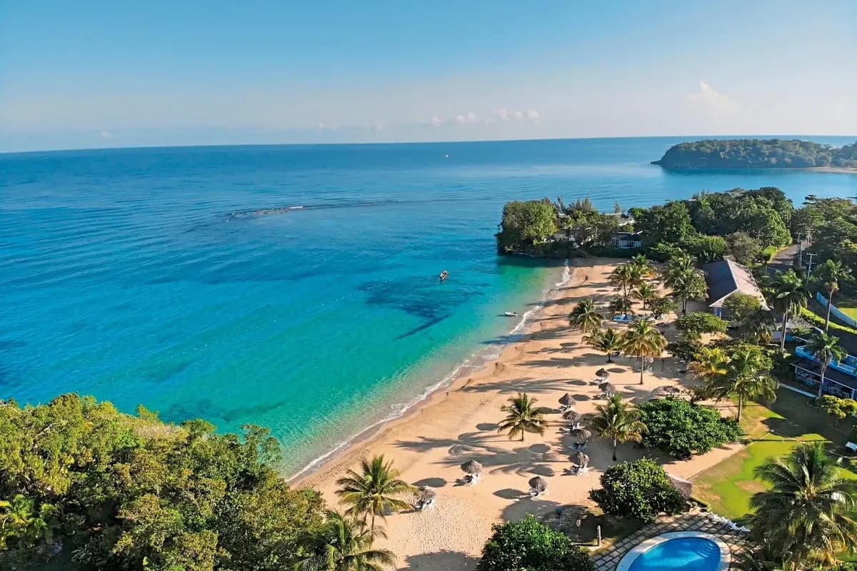 Widok z góry na piaszczystą plażę hotelu Jamaica Inn w Ocho Rios z parasolami ze strzechy, palmami i turkusowym Morzem Karaibskim