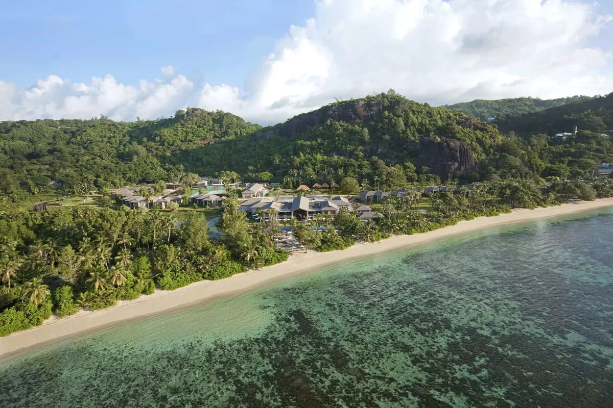 Hotel Kempinski Seychelles Resort na Mahé z lotu ptaka: piaszczysta plaża, płytka laguna i zalesione wzgórza z granitowymi skałami