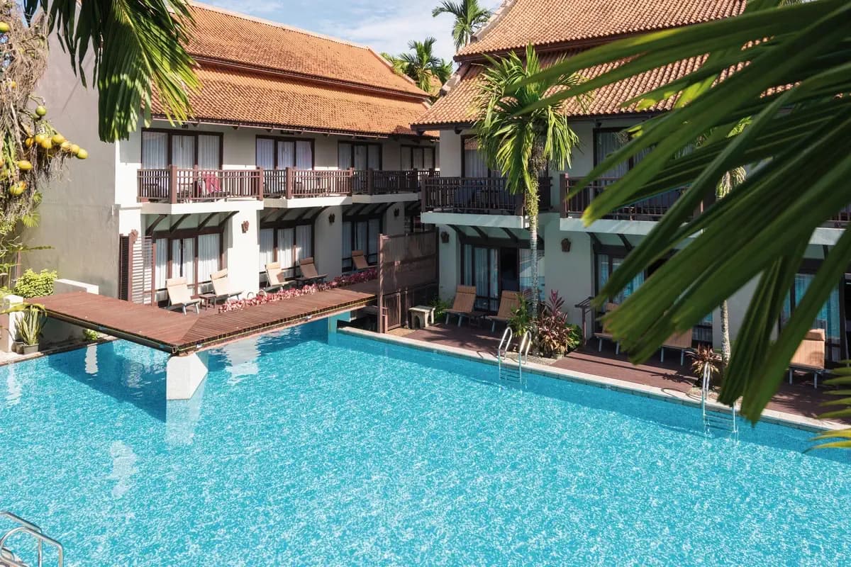 Basen hotelu Khaolak Bhandari Resort & Spa w Khao Lak w Tajlandii, otoczony piętrowymi budynkami z drewnianymi balkonami i palmami