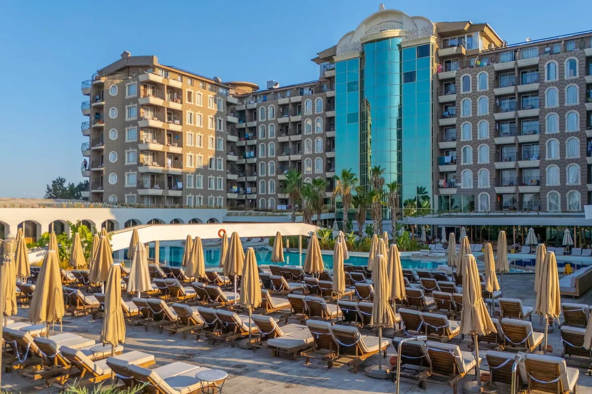 Leżaki i złożone parasole przy basenie hotelu Laur Experience Elegance w Didim, w tle wielopiętrowe budynki hotelowe z przeszkloną wieżą