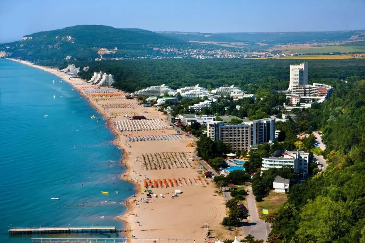 Albena z lotu ptaka: długa, szeroka plaża z rzędami parasoli, hotele wśród zielonego lasu na zboczu i spokojne, niebieskie Morze Czarne