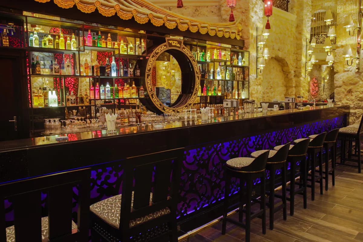 Bar w hotelu Pickalbatros Citadel w Sahl Hasheesh: podświetlone półki z butelkami alkoholi, długa lada i wysokie hokery
