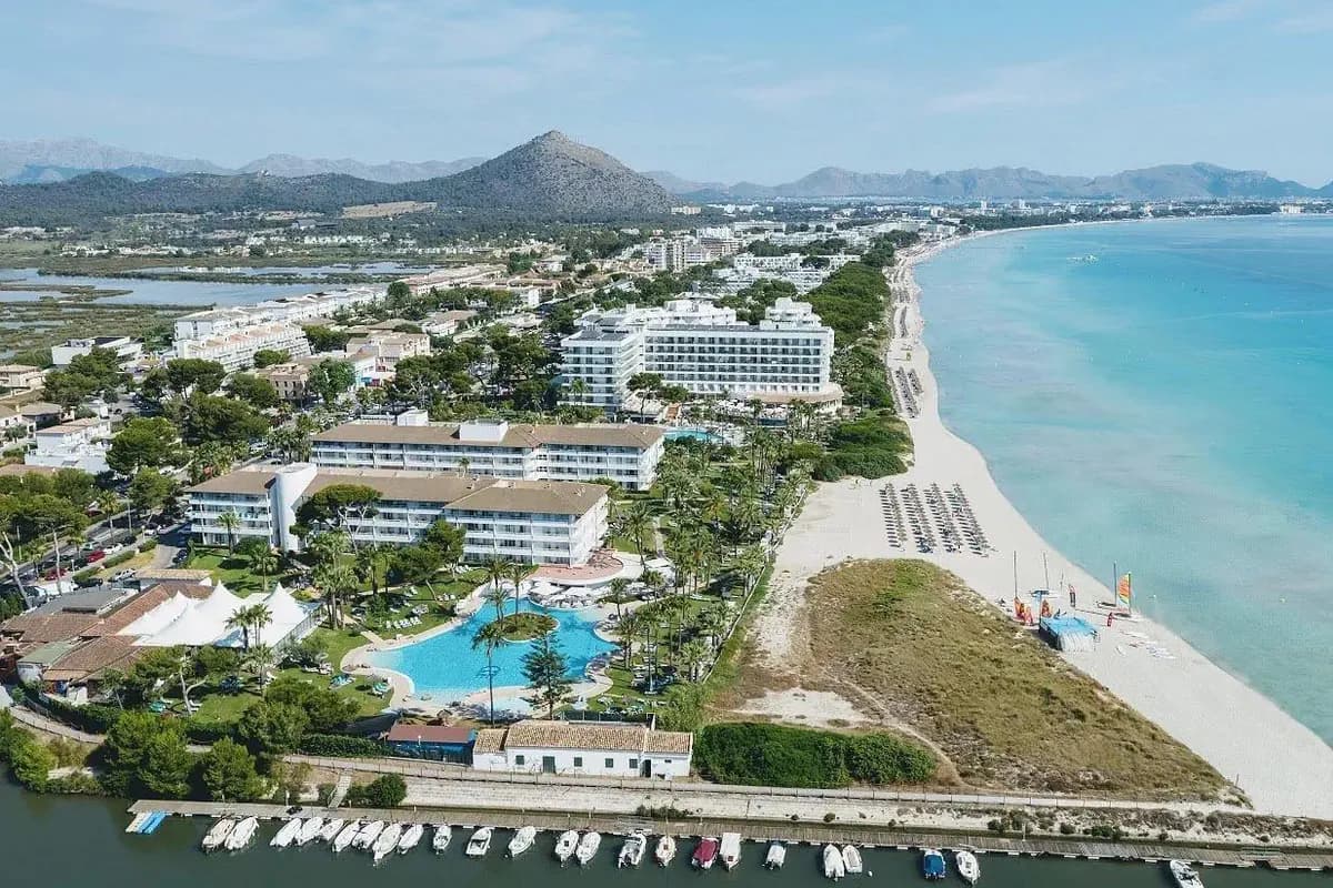 Długa, jasna plaża w Playa de Muro na północy Majorki, hotele wśród palm, a w tle góry i lagunowe rozlewiska