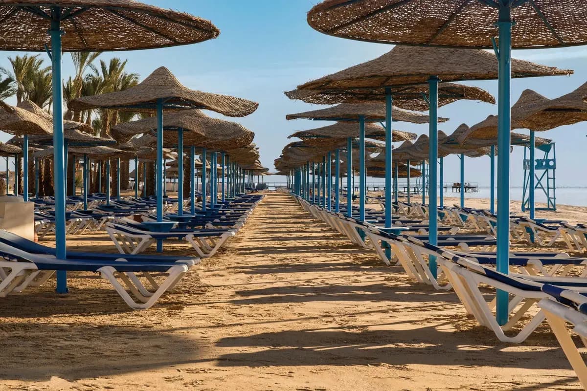 Plaża hotelu Radisson Individuals Marina w Port Ghalib koło Marsa Alam: rzędy leżaków w cieniu słomianych parasoli, w tle molo i Morze Czerwone
