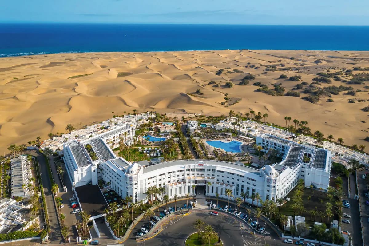 Hotel Riu Palace Maspalomas na Gran Canarii z lotu ptaka: białe budynki z basenami i palmami, za nimi wydmy Maspalomas i ocean