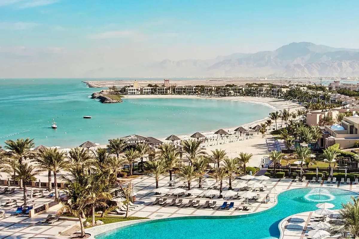 Hotel Rixos Al Mairid w Ras al-Chajmie: basen wśród palm, zatoka z jasną plażą i turkusową wodą, a w tle góry Hadżar