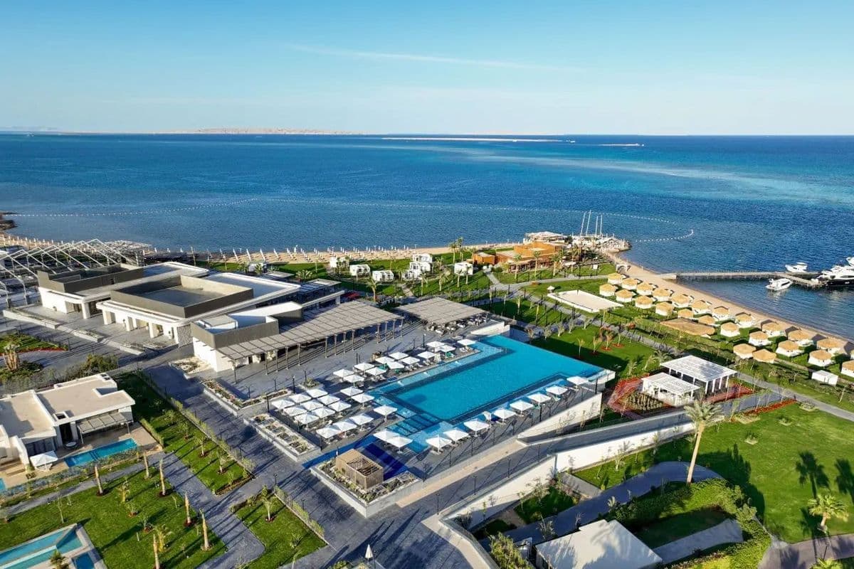 Widok z góry na hotel Rixos Premium Magawish w Hurghadzie z basenem, plażą i pomostem, przy którym cumują łodzie motorowe