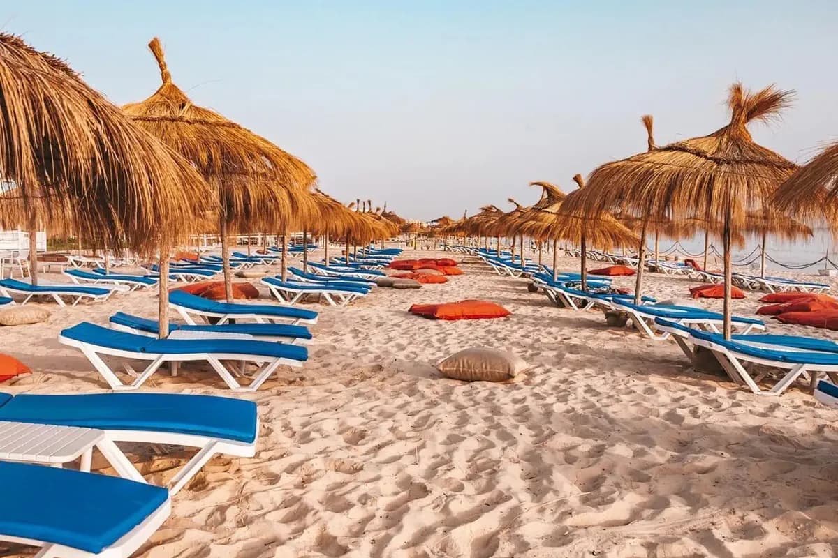 Piaszczysta plaża hotelu Sousse Pearl Marriott Resort & Spa w Tunezji z rzędami niebieskich leżaków i parasolami ze słomy