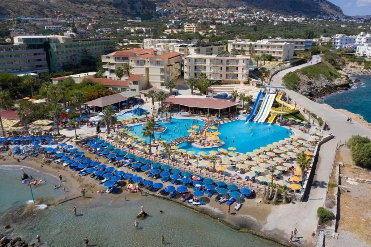 Hotel Sunbay na Krecie z lotu ptaka: basen ze zjeżdżalniami, wysepką i mostkami, rzędy parasoli oraz mała plaża nad płytką zatoczką