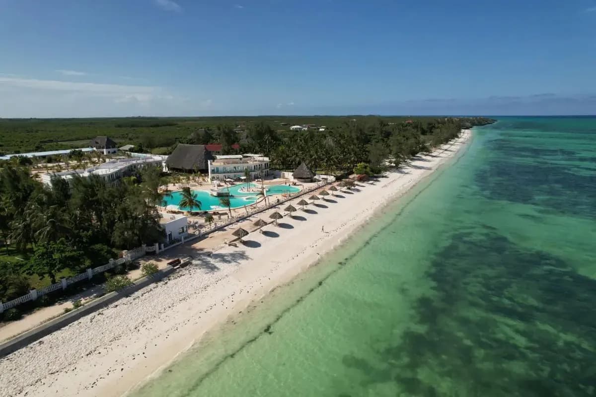 Widok z lotu ptaka na hotel The One Resort na Zanzibarze: baseny, parasole kryte strzechą, długa biała plaża i płytka, turkusowa woda z ciemnymi plamami rafy