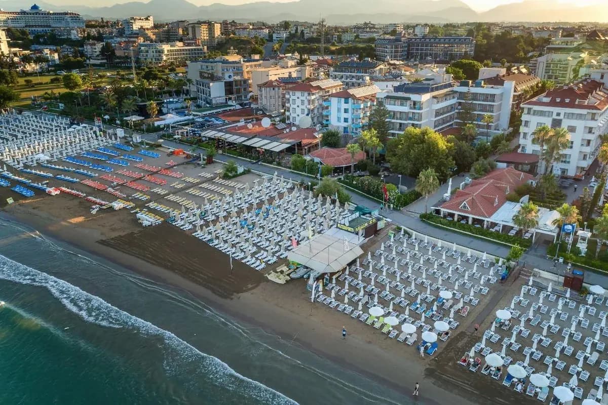 Plaża w Side z lotu ptaka: rzędy leżaków i parasoli nad brzegiem morza, za nimi hotele, a w oddali góry