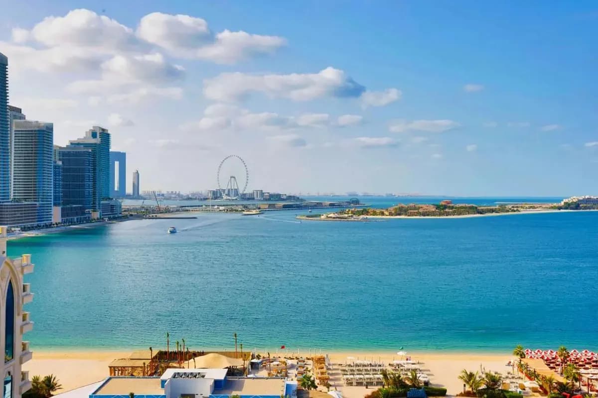 Widok z hotelu Tumbi na Palm Jumeirah w Dubaju: piaszczysta plaża, turkusowa zatoka, wieżowce przy plaży JBR i diabelski młyn Ain Dubai